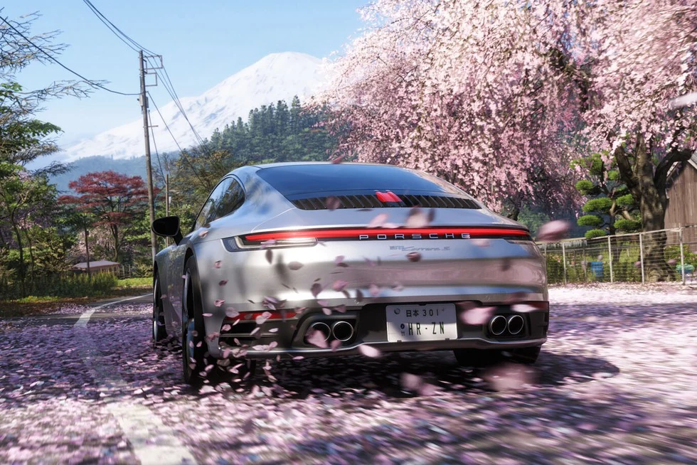 Silver sports car driving along a cherry blossom-lined road